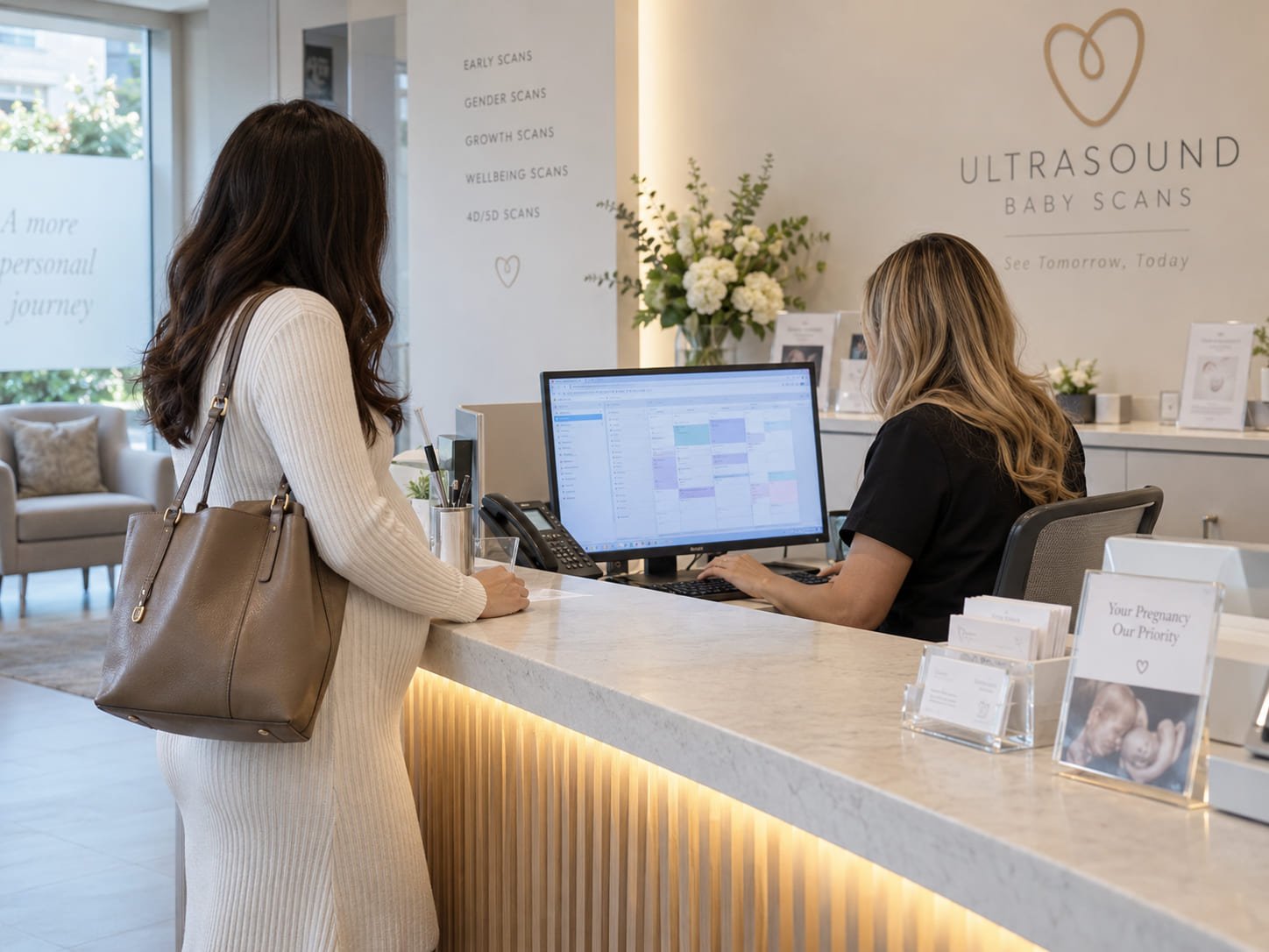 Receptionist at a private pregnancy scan clinic booking a follow-up appointment for an expectant mother at the front desk